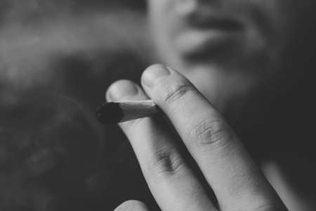 joint in man hand. A man smokes cannabis weed, a . Smoke on a black background. Concepts of medical marijuana use and legalization of the cannabis. On a black backgroundの写真素材