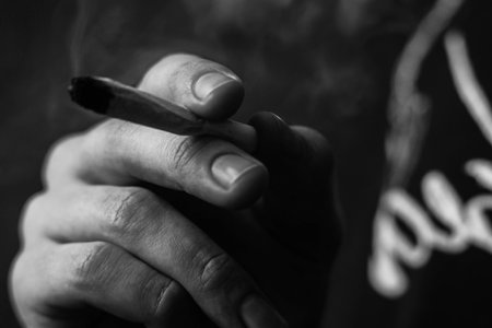 cannabis weed, a joint in his hands A man smokes . Smoke on a black background. Concepts of medical marijuana use and legalization of the cannabis. On a black backgroundの写真素材
