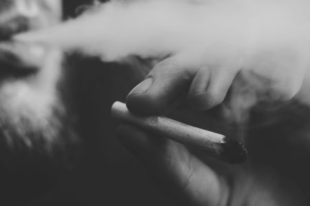cannabis weed A man smokes, a joint and a lighter in his hands. Smoke on a black background....