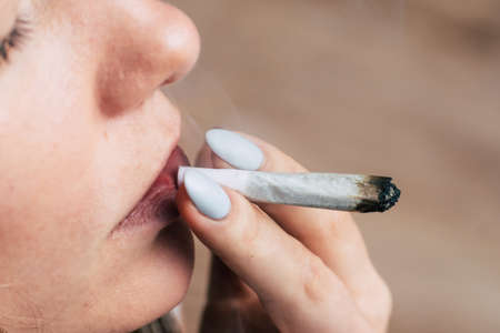 smokes cannabis weed, a joint and a lighter in his hands. Smoke on a black background. Concepts of medical marijuana use and legalization of the cannabis. On a black backgroundの写真素材