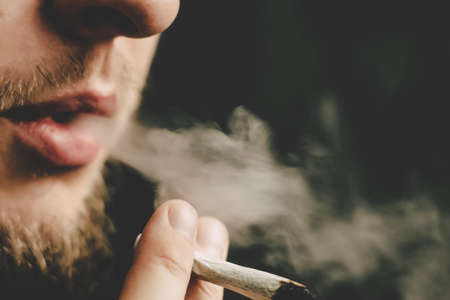 joint in man hand. A man smokes cannabis weed, a . Smoke on a black background. Concepts of medical marijuana use and legalization of the cannabis. On a black backgroundの写真素材