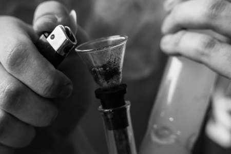 A man smokes cannabis weed, a joint and a lighter in his hands. Smoke on a black background. Concepts of medical marijuana use and legalization of the cannabis. On a black backgroundの写真素材