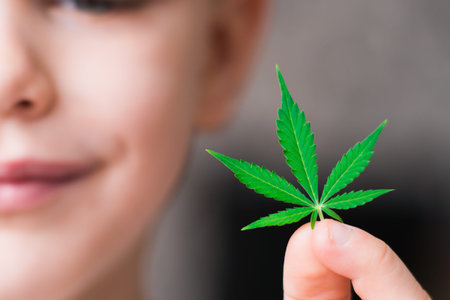 Smiling kid child holding a hemp leaf. Concepts of using marihuna for medicinal purposes for children, Medical use of non-psychoactive cannabidiol CBDの写真素材