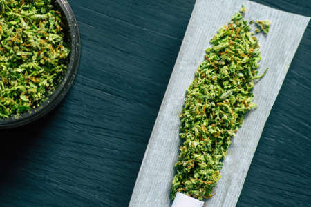 Grinder with crushed cannabis flowers and not twirled jamb on the background of a black wooden tableの写真素材
