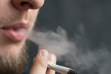 A man smokes weed cannabis a joint and a lighter in his hands. Smoke on a black background. Concepts...