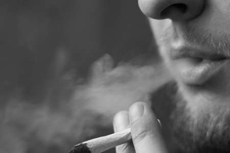 A man smokes cannabis weed, a joint and a lighter in his hands. Smoke on a black background. Concepts of medical marijuana use and legalization of the cannabis. On a black backgroundの写真素材