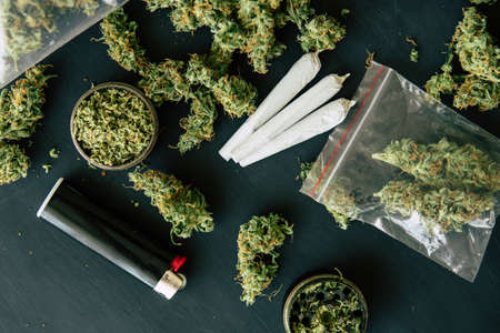 Bud of marijuana flowers on scales, grinder and shredded cannabis joint and a packet of weed and Smartphone on a black wood backgroundの写真素材