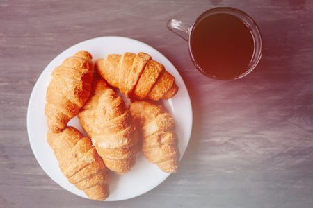 Coffee cup and fresh baked croissants on wooden background. Top View.