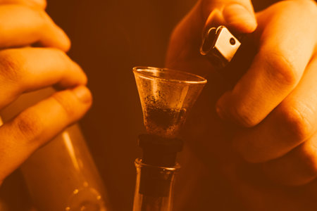 A man smokes cannabis weed, a joint and a lighter in his hands. Smoke on a black background....