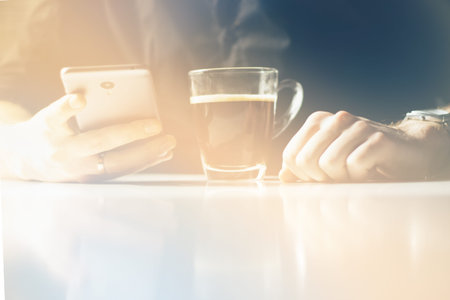 Young man having morning coffee and reading news in his smartphoneの写真素材