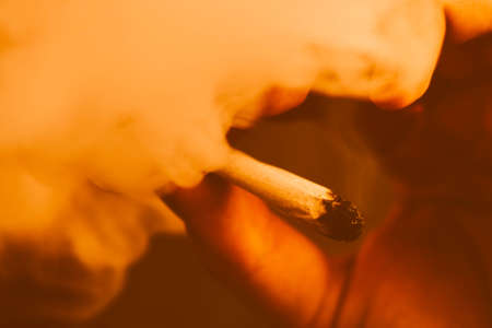 cannabis weed A man smokes, a joint and a lighter in his hands. Smoke on a black background. Concepts of medical marijuana use and legalization of the cannabis. On a black backgroundの写真素材