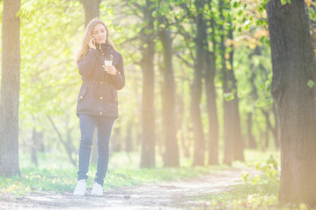 A girl is walking in the morning in a park with a smartphone and coffeeの写真素材