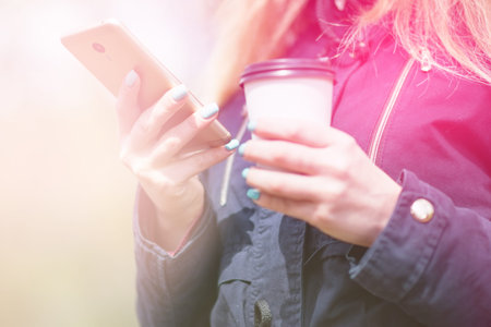 A girl is walking in the morning in a park with a smartphone and coffee