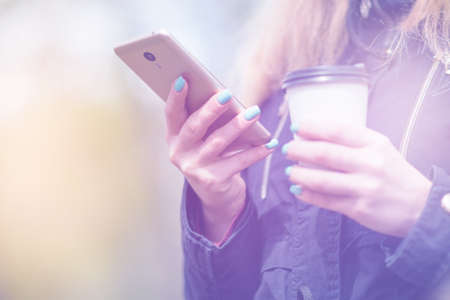 A girl is walking in the morning in a park with a smartphone and coffeeの写真素材
