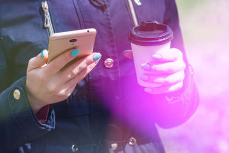 A girl is walking in the morning in a park with a smartphone and coffeeの写真素材