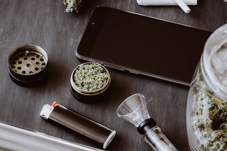 Cannabis buds on the scales lie on the table with a grinder, joint and smartphone. Marijuana in the...