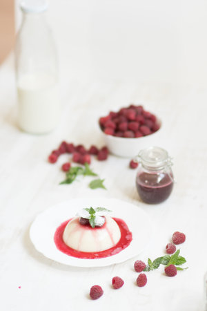 Light background. Close up. Flying powdered sugar. Panakota with raspberries and mint. Vertical...