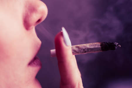 cannabis weed A woman smokes, a joint and a lighter in his hands. Smoke on a black background. Concepts of medical marijuana use and legalization of the cannabis. On a black backgroundの写真素材