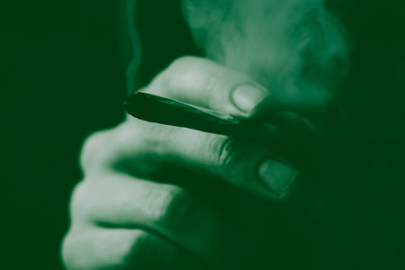 joint in man hand. A man smokes cannabis weed, a . Smoke on a black background. Concepts of medical...