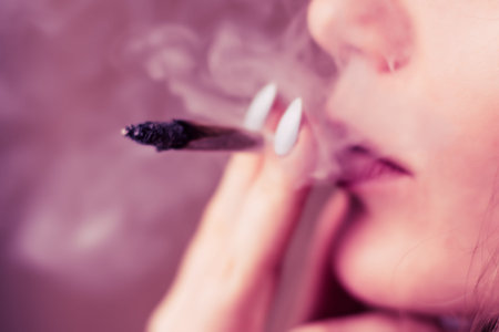 Smokes cannabis weed, a joint and a lighter in his hands. Smoke on a black background. Concepts of...