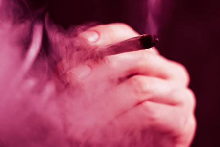 A man smokes weed cannabis a joint and a lighter in his hands. Smoke on a black background. Concepts...