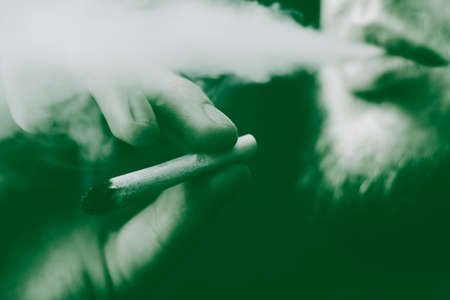 a joint in hand A man smokes cannabis weed, . Smoke on a black background. Concepts of medical marijuana use and legalization of the cannabis. On a black backgroundの写真素材