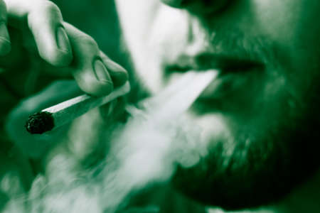 cannabis weed, a joint in his hands A man smokes . Smoke on a black background. Concepts of medical marijuana use and legalization of the cannabis. On a black backgroundの写真素材