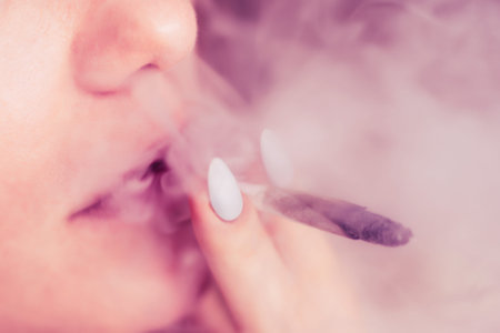joint in woman hand. A woman smokes cannabis weed, a . Smoke on a black background. Concepts of...