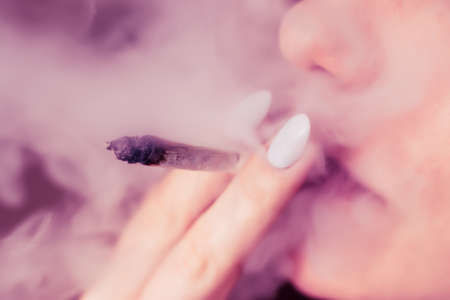 A woman smokes cannabis weed, a joint and a lighter in his hands. Smoke on a black background. Concepts of medical marijuana use and legalization of the cannabis. On a black backgroundの写真素材