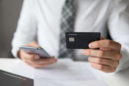 Smartphone and Internet Commerce. Online payments through the phone. Young businessman with a bank credit card in his hands. Payment of goods online. Online trading on the currency exchange.の写真素材