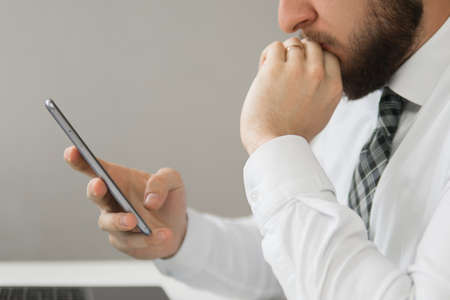 Young bearded businessman. Light background. Financial business. Holding smartphone in hand. Office work with a laptop.の写真素材