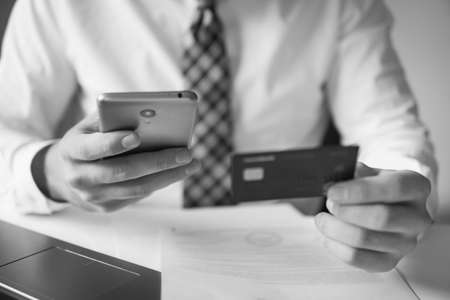 Young businessman with a bank credit card in his hands. Payment of goods online. Online payments through the phone. Online trading on the currency exchange. Smartphone and Internet Commerce.の写真素材