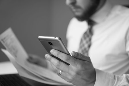 Office work with a laptop. Smartphone in hand. Close up. Young bearded businessman. Businessman work with computer on table in office work. Financial business. Light background.の写真素材