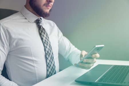 Financial business. Office work with a laptop. Businessman work with computer on table in office work. Light background. Close up. Smartphone in hand Young bearded businessman.の写真素材