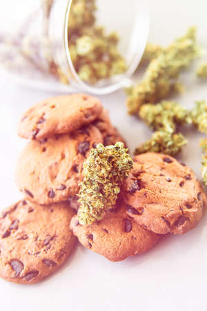 Treatment of medical marijuana for use in food, white background. Cookies with cannabis herb CBD. Cookies with cannabis and buds of marijuana on the table. Vertical shot light leaksの写真素材