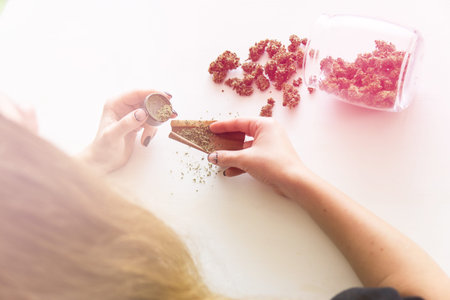 Woman preparing and rolling marijuana cannabis joint. Woman rolling a marijuana blunt on white...