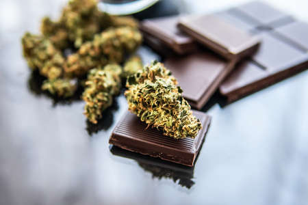 Chocolate with cannabis and buds of marijuana on the table. Treatment of medical marijuana for use in food, black background. Concept of chocolate with cannabis herb CBD.の写真素材