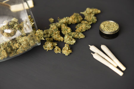 Cannabis buds on black table, joint with weed, grinder with fresh marijuana, top view, close up,