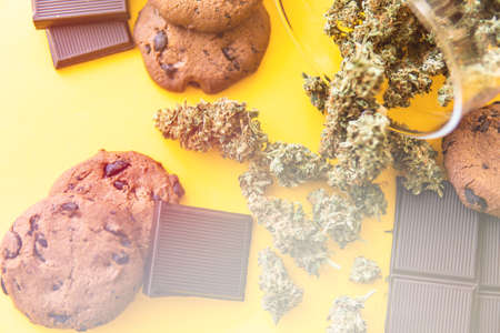 Cookies and Chocolate with weed and buds of marijuana on the table. Cannabis CBD herb Chocolate and Cookies. Treatment of medical marijuana for use in food, yellow background. light leaksの写真素材