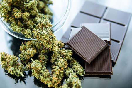 Concept of chocolate with cannabis herb CBD. Treatment of medical marijuana for use in food, black background. Chocolate with cannabis and buds of marijuana on the table.の写真素材