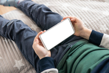 Smartphone with a white screen in hand child. Smartphone with a mock up in the hands of a child. Phone a for mock up is holding kid. top view close upの写真素材