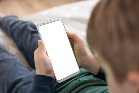 Phone a for mock up is holding kid. Smartphone with a white screen in hand child. Smartphone with a mock up in the hands of a child. top view close upの写真素材