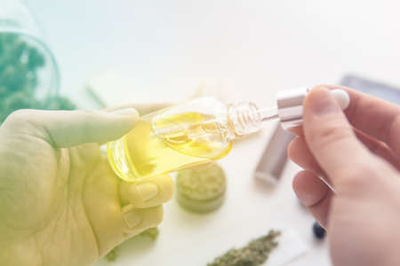 CBD cannabis OIL on white background, medical marijuana concept, close up, bottle of oil Cannabis in pipette in hand, hemp product, light leaks color tonesの写真素材