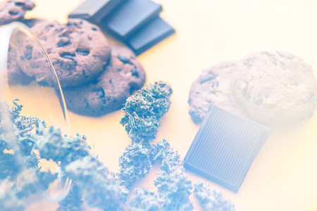 Cannabis CBD herb Chocolate and Cookies. Cookies and Chocolate with weed and buds of marijuana on the table. Treatment of medical marijuana for use in food, yellow background. light leaksの写真素材