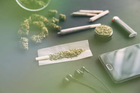 close up, grinder in hand with fresh Cannabis, joint with weed, marijuana buds on black table, light leaks color tonesの写真素材