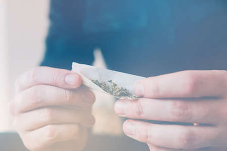 Drugs narcotic concept. Man rolling a marijuana joint. Man preparing and rolling marijuana cannabis joint. Drug use. Close up . Close up of addict lighting up marijuana joint with lighter.の写真素材