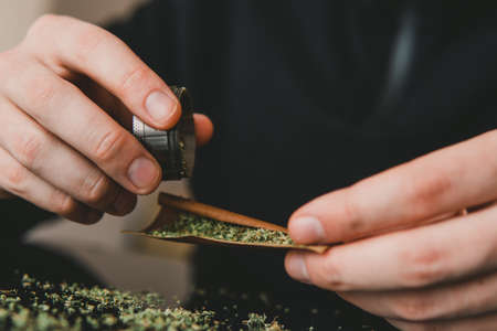 Man rolling marijuana cannabis blunt. Man rolling a marijuana weed blunt. Close up marijuana joint with lighter.の写真素材