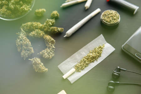 marijuana buds on black table, close up, grinder in hand with fresh Cannabis, joint with weed, light leaks color tonesの写真素材