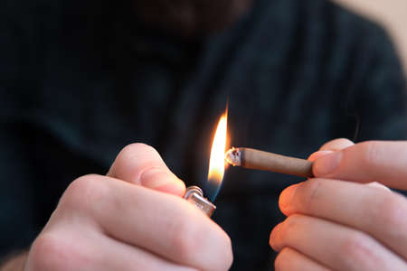 Man preparing and rolling marijuana cannabis Blunt. Drugs narcotic concept. Close up. Close up of addict lighting up marijuana Blunt with lighter. Man rolling a marijuana Blunt Drug use.の写真素材