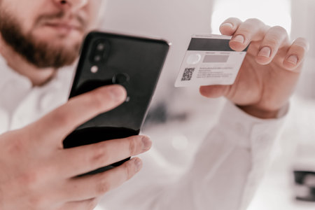 Online shopping concept in morning light. Close up hands holding credit card and using mobile smart...